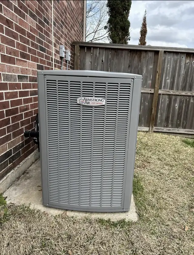 Armstrong Air condenser on a pad beside a brick wall and a wooden fence